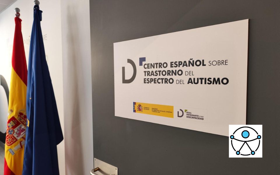 Fotografía de la puerta de entrada del Centro Español de Autismo con su logo y las banderas de España y de la Unión Europea, al fondo. En la esquina inferior derecha el logo de la accesibilidad universal.