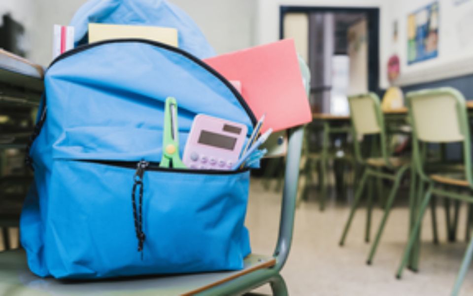 Fotografía de una mochila encima de una silla dentro de un aula de escuela.
