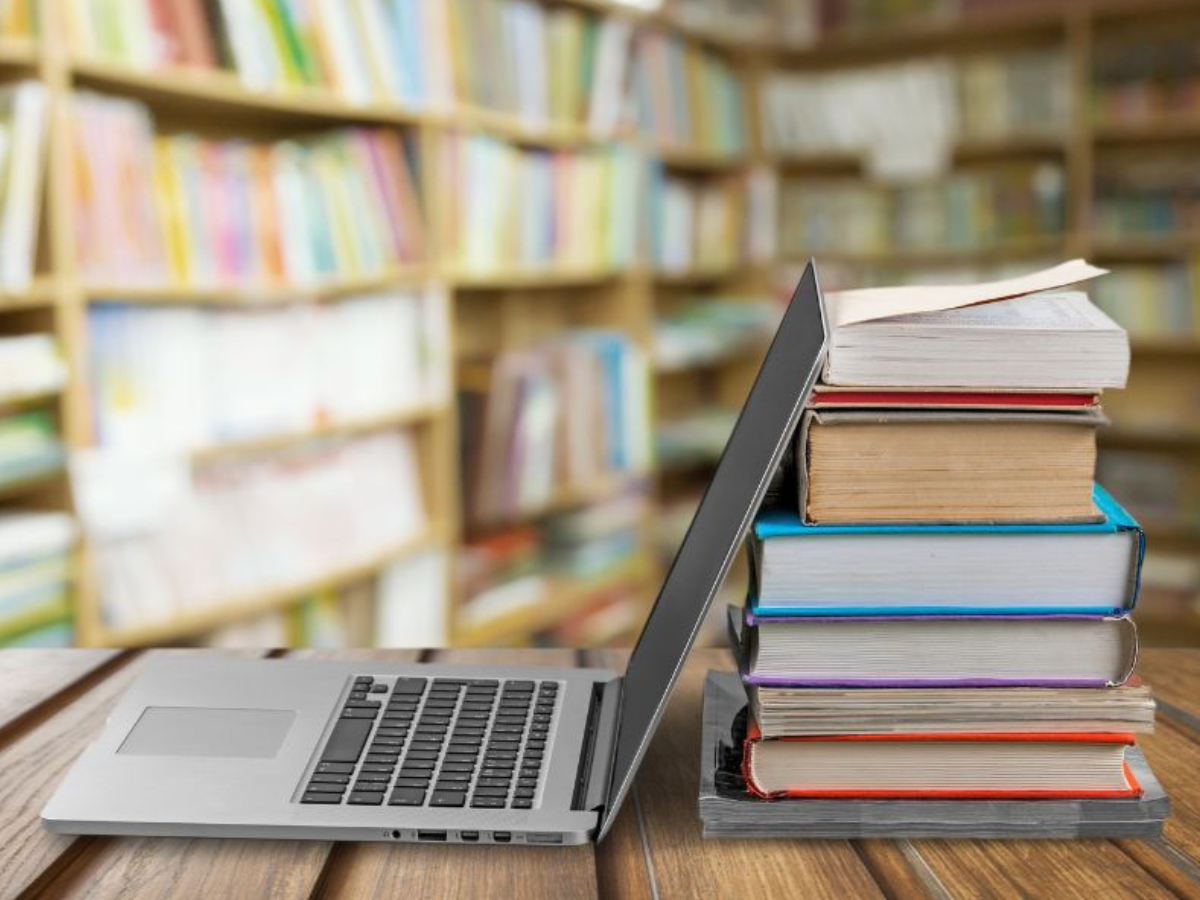 Un ordenador portatil apoyado en unos libros, todos sobre una mesa en una sala de biblioteca