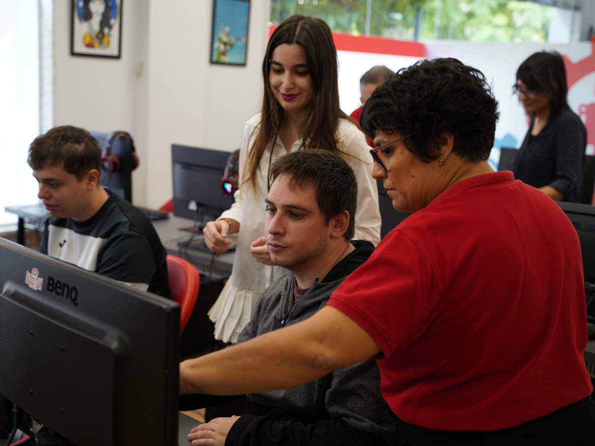 un grupo de personas en un aula frente a unos ordenadores con una persona señalando la pantalla